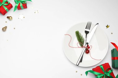 Beyaz arka planda tabak, çatal bıçak takımı ve şenlik dekoruyla Noel sofrası. Metin için boşluk