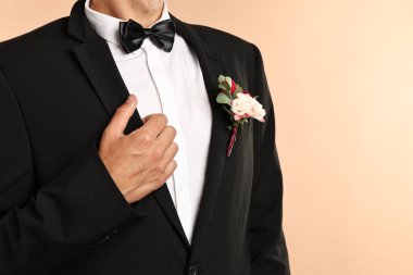 Groom in suit with stylish boutonniere on beige background, closeup. Space for text clipart