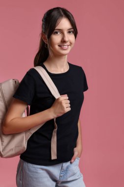 Pembe arka planda sırt çantalı sevimli genç kız portresi.