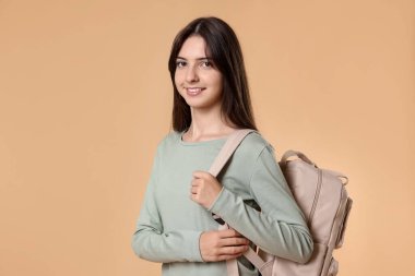 Bej arka planda sırt çantalı gülümseyen genç kızın portresi.