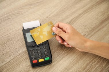 Kredi kartı olan bir kadın ahşap masada terminal kullanıyor, yakın plan.