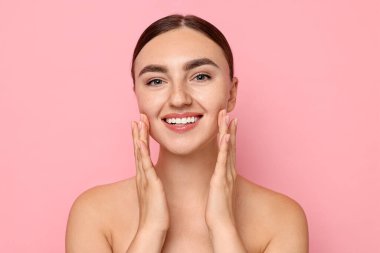 Yüz masajı. Pembe arka planda sağlıklı ciltli güzel bir kadın.