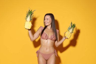 Turuncu arka planda ananas parçaları olan bikinili çekici bir kadın.