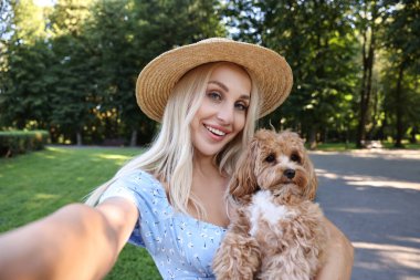 Güzel genç bir kadın parkta sevimli bir köpekle selfie çekiyor.