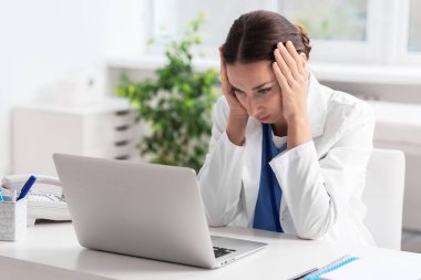 Klinikteki dizüstü bilgisayarlı beyaz masadaki yorgun hemşire.