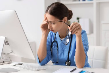 Klinikteki beyaz masada gözlüklü yorgun hemşire.
