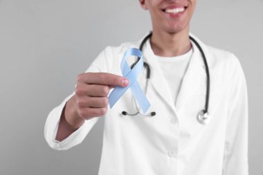 Prostat kanseri farkındalığı. Gri arkaplan ve seçici odak noktasında açık mavi kurdele tutan doktor