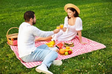 Dışarıda piknik battaniyesinde meyve suyu bardakları tokuşturuyorlar.