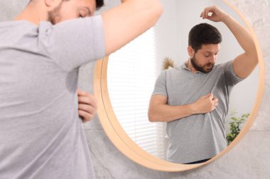 Evde aynanın yanında deodorant kullanmadan önce tişörtlü duygusal bir adam.