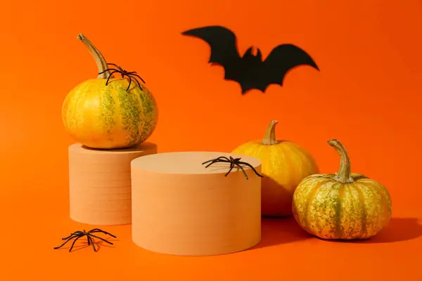 Stock image Halloween celebration. Pumpkins, black paper bat, spiders and podiums on orange background