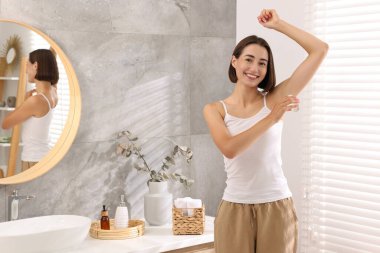 Gülümseyen kadın banyoya deodorant sürüyor.