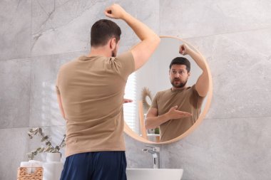 Evde aynanın yanında deodorant kullanmadan önce tişörtlü duygusal bir adam.
