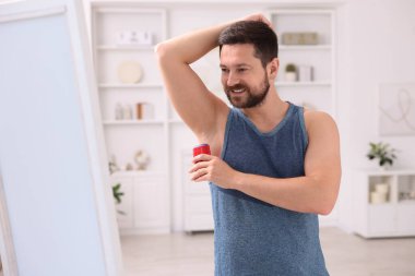 Gülümseyen adam evde katı deodorant sürüyor.