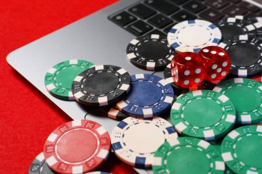 Poker fişleri, dizüstü bilgisayar ve zarlar kırmızı masada, yakın plan. Çevrimiçi oyun