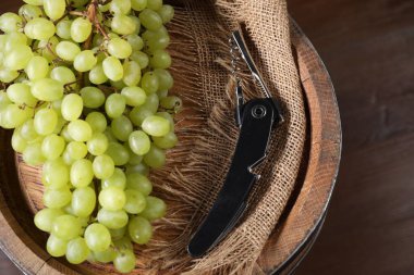 Tirbuşonlu sommelier bıçağı, üzümler ve ahşap fıçı masada, yakın plan.