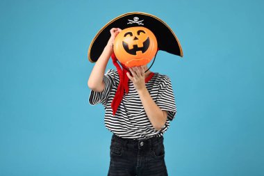 Açık mavi arka planda, korsan gibi giyinmiş balkabağı kovalı çocuk. Cadılar Bayramı kostümü