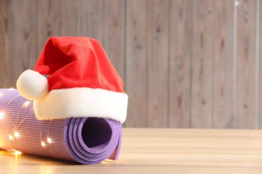 Noel ışıkları ve tahta yüzeyinde Noel Baba şapkası olan yoga minderi. Metin için boşluk