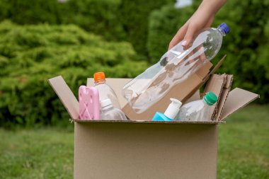 Geri dönüşüm konsepti. Dışarıdaki karton kutuya plastik şişe koyan kadın, yakın plan.