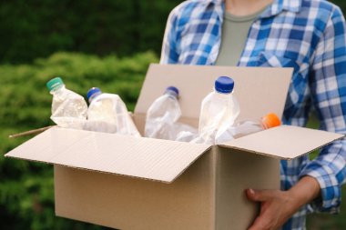 Geri dönüşüm. Elinde plastik şişelerle karton kutu tutan kadın, yakın plan.