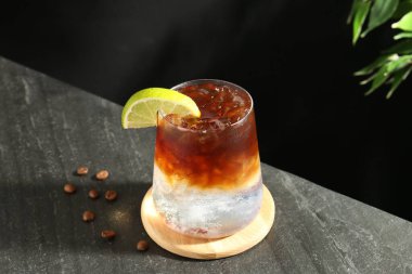 Koyu masada limon dilimi ve kahve çekirdeği ile espresso toniği tazeleniyor.