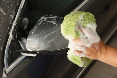 Oto yıkayan adam araba yıkamada süngerle yıkıyor.