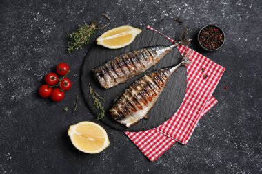 Lezzetli ızgara uskumru, kekik, limon ve domatesler koyu dokulu masa, düz uzanma