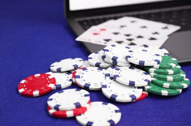 Laptop, poker fişleri ve mavi masada iskambil kağıtları, yakın plan. Çevrimiçi oyun
