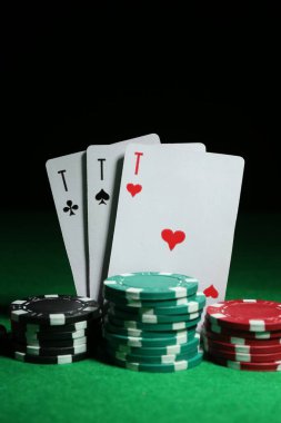 Koyu arkaplana karşı yeşil masada kart ve poker çipleri oynamak