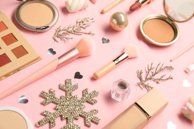 Farklı makyaj fırçaları, dekoratif kozmetik ürünleri ve pembe arka planda Noel dekorasyonu.