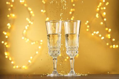 Bulanık ışıklarla altın arka plana karşı köpüklü şarap ve konfeti bardakları. Noel dekoru