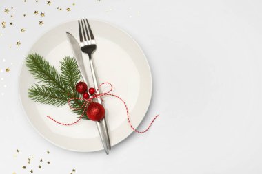 Beyaz arka planda tabak, çatal bıçak takımı ve şenlik dekoruyla Noel sofrası. Metin için boşluk