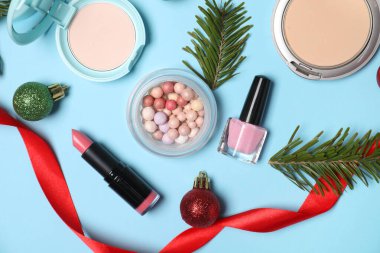 Açık mavi arka planda makyaj ürünleri ve Noel dekoruyla düz konum
