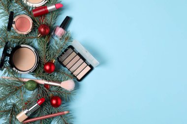 Açık mavi zemin üzerinde makyaj ürünleri ve Noel dekoru ile düz konum, metin için boşluk