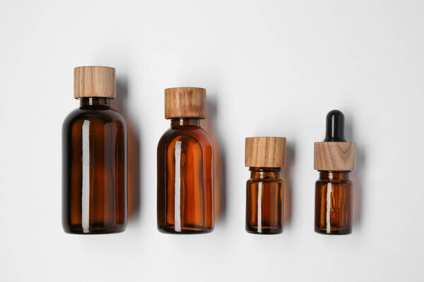 Bottles of essential oils on white background, flat lay