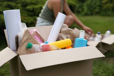 Geri dönüşüm. Karton kutunun yanında farklı çöp kutuları olan, seçici odaklı bir kadın.