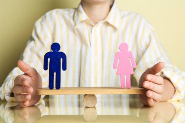 Gender equality concept. Woman with male and female figures on scales against light yellow background, closeup clipart