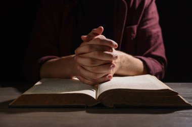 İncilli bir adam ahşap masada dua ediyor, yakın plan.