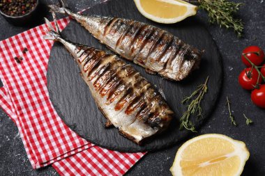 Lezzetli ızgara uskumru, kekik, limon ve domatesler koyu dokulu masada.