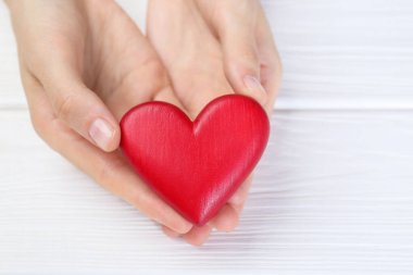 Beyaz ahşap masada kırmızı kalbi tutan kadın, yakın plan.