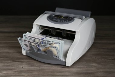 Tahta masanın üzerinde dolar banknotları olan para sayma makinesi.