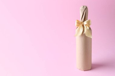 Pembe arka planda saten fiyonklu çuval içinde şarap şişesi. Metin için boşluk