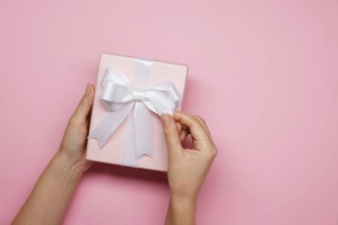 Pembe arka planda fiyonklu hediye kutusu dekorasyonu yapan kadın, üst manzara. Metin için boşluk