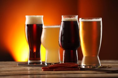 Farklı tipte bira ve aperatiflerle dolu bardaklar ahşap masa üzerinde renk arka planına karşı