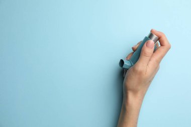 Açık mavi arka planda astım spreyi tutan bir kadın. Metin için boşluk