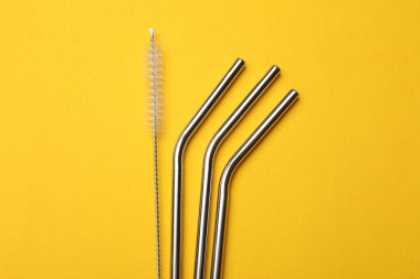 Metal pipetler ve sarı arka planda temizlik fırçası, düz yatıyordu.