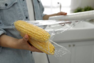 Mutfakta mısır koçanlarının üzerine plastik yiyecek saran kadın, yakın plan.