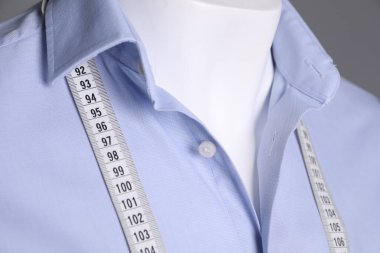 Male mannequin with light blue shirt and measuring tape on grey background, closeup clipart