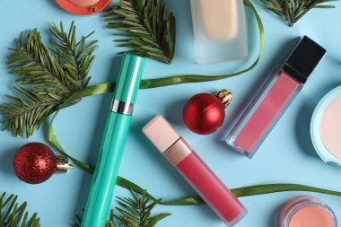 Açık mavi arka planda makyaj ürünleri ve Noel dekoru, düz konum