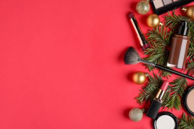 Kırmızı zemin üzerinde makyaj ürünleri ve Noel dekoru olan düz konum, metin için boşluk