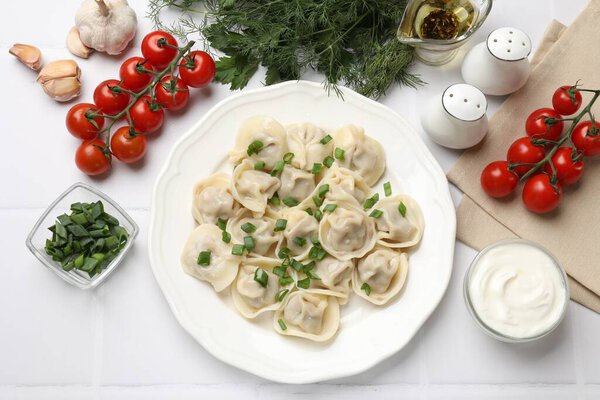 Вкусные пельмени с зеленым луком, подаваемые на белом плиточном столе, плоской раскладкой